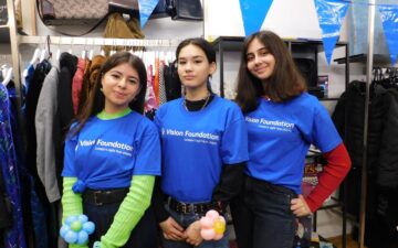 Three young women volunteers stand together in bright blue Vision Foundation t-shirts
