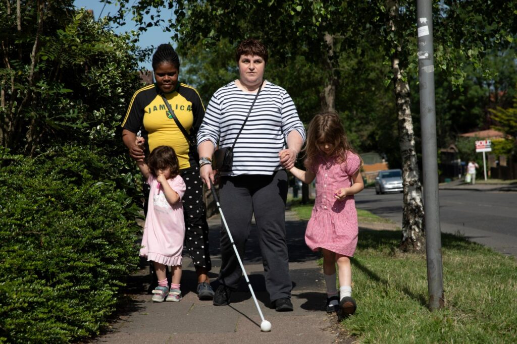 Charmaine uses her cane to guide her as she walks her two daughters home from school with their childminder Rita. 