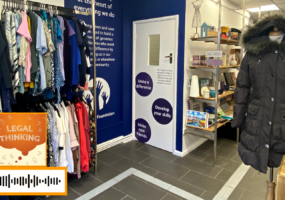 Inside of our West Norwood charity shop. Showing a neat rack of clothes and a clear, tactile pathway leading through the shop. The scannable Spotify code for the podcast is on the image.