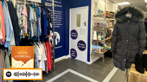 Inside of our West Norwood charity shop. Showing a neat rack of clothes and a clear, tactile pathway leading through the shop. The scannable Spotify code for the podcast is on the image.