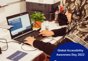 Khafsa sat at desk using access technology. Text: Global Accessibility Awareness Day 2022