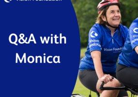 Monica is smiling widely on the back of a tandem bicycle, riding through a lush green park. She's wearing a blue Vision Foundation cycling jersey with a red helmet. Text: Q&A with Monica