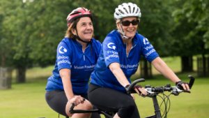 Monica and HRH The Countess of Wessex smiling widely whilst cycling on a tandem together