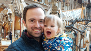 Olly holding Harper for a smiley selfie in front of some dinosaur skeletons.