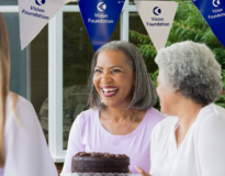 Two mature women at a bake sale, behind them is Vision Foundation bunting