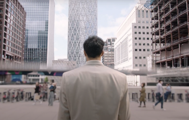 Naqi, stood facing Canary Wharf, he is surrounded by skyscrapers