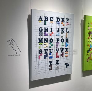 The Braille decoder art piece with the "please do touch" sign beside it.