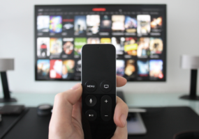 A hand holding a remote in front of a blurred tv screen