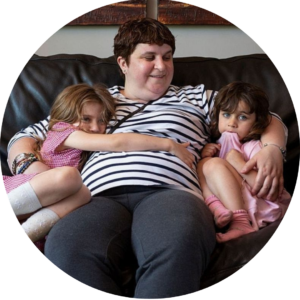Charmaine sitting on the sofa with daughters, Alex and Sophia nestled in either side of her. She smiles down ay them both.