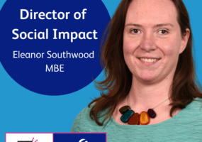 Text: Director of Social Impact, Eleanor Southwood MBE. ID: Headshot of Eleanor, against a blue background. Eleanor is a white woman with dark brown hair which falls past her shoulders. She is wearing a teal green jumper with a colourful chunky beaded necklace.