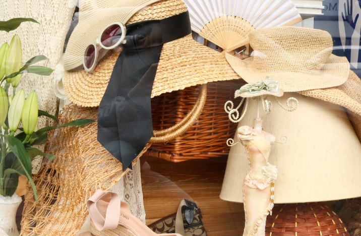 Shop window full of donated items including a hand fan, sunglasses, a straw hat and a jewellery holder.