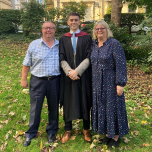Josh, wearing a graduation gown, with his parents stood either side of him.