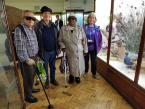Four people standing beside a museum display, looking towards the camera. Two of these people use canes.