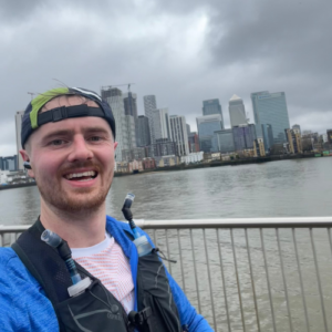 A photo of Paul smiling into the camera, in the distance the London skyline under a cloudy sky.