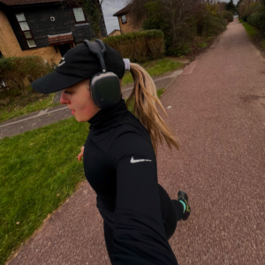 A selfie taken by Courteney while running on the pavement. She has long hair tied up and is wearing running gear.